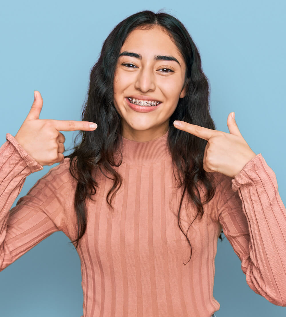 smiling young woman with braces pointing to mouth