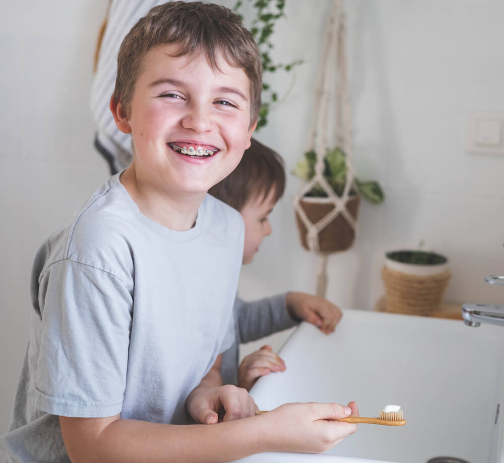 smiling young boy with braces at sink holding toothbrush